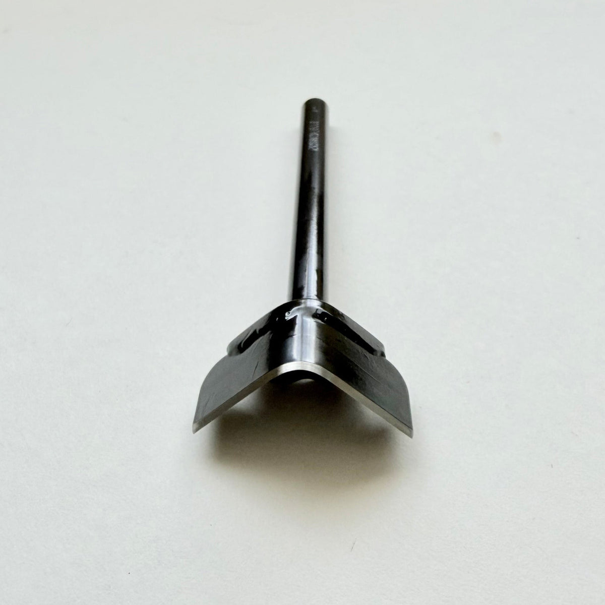 A black metal corner punch for leather with a long straight black handle, photographed on a plain light grey background.