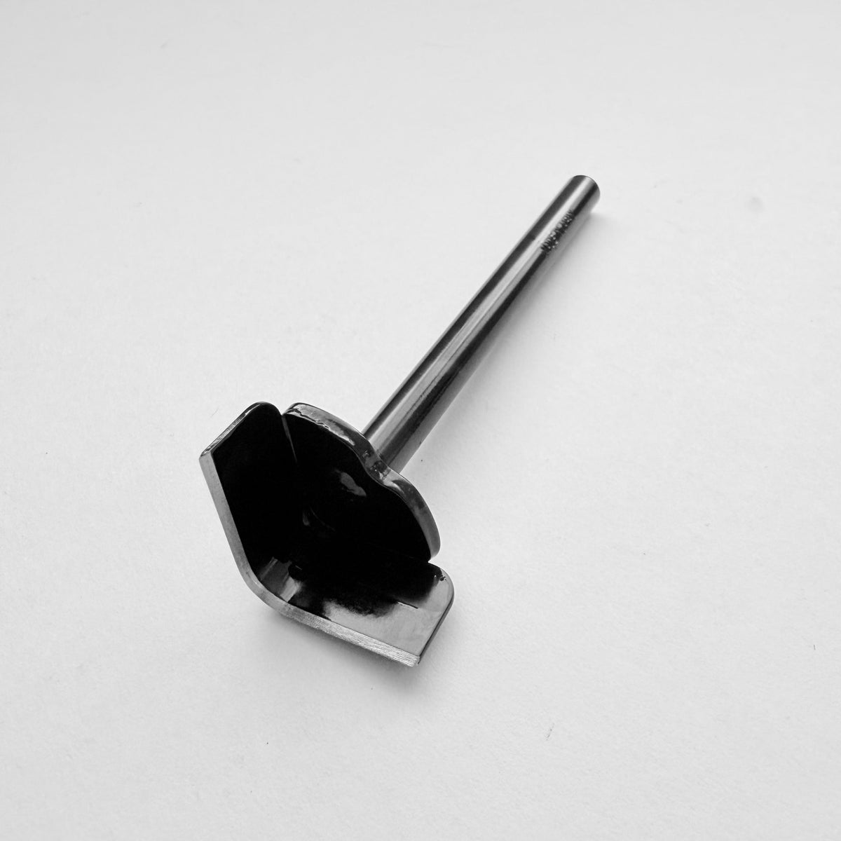 A black metal corner punch for leather with a long straight black handle, photographed on a plain light grey background.