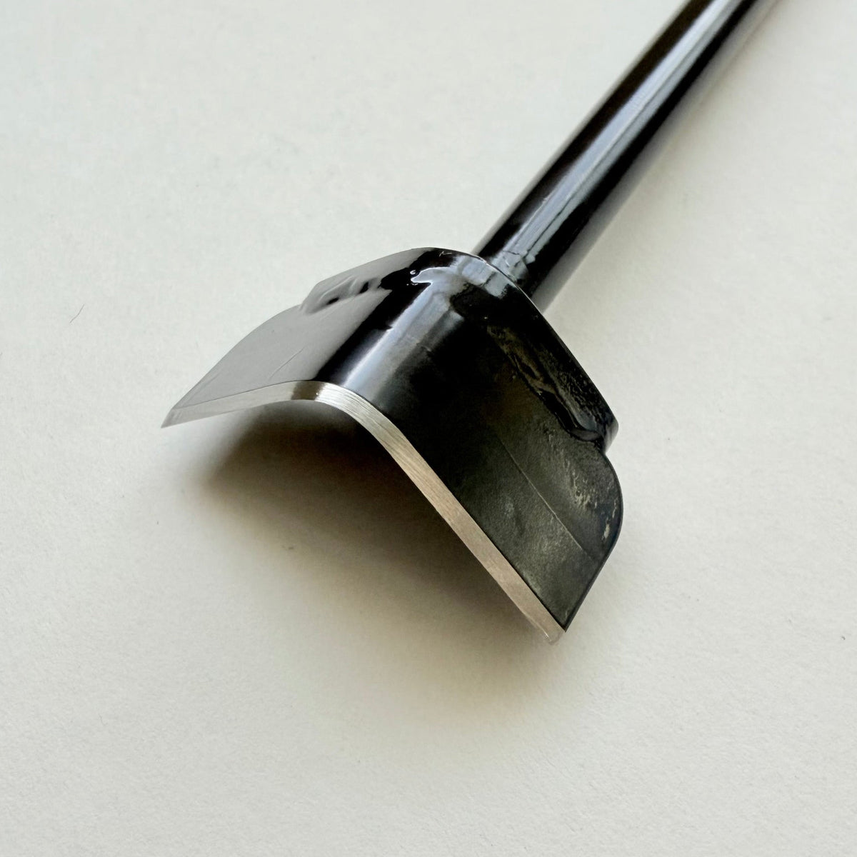 A black metal corner punch for leather with a long straight black handle, photographed on a plain light grey background.