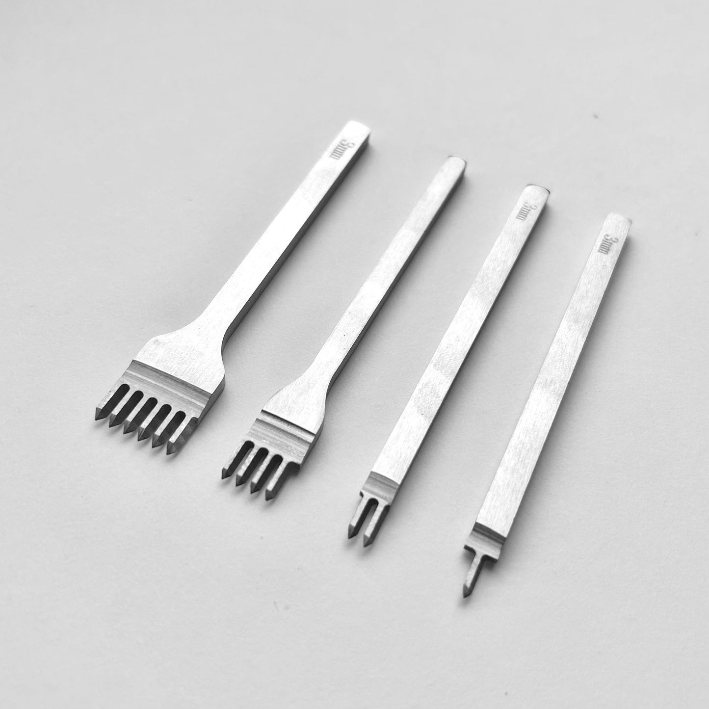 Set of four metal leather stitching punches on a light grey background