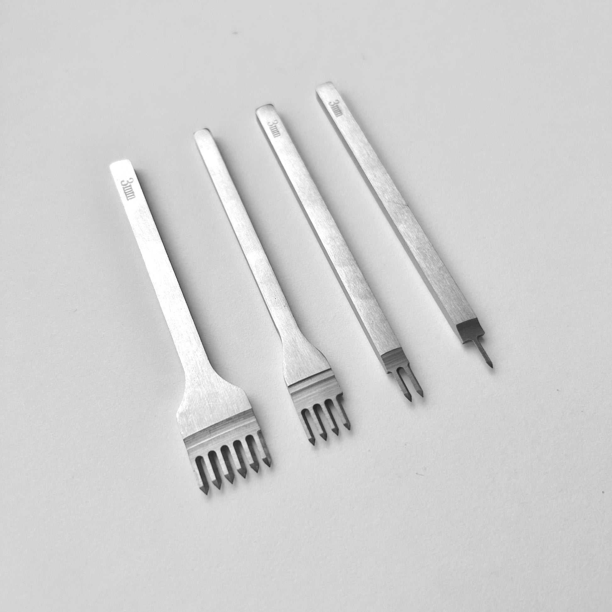 Set of four metal leather stitching punches on a light grey background