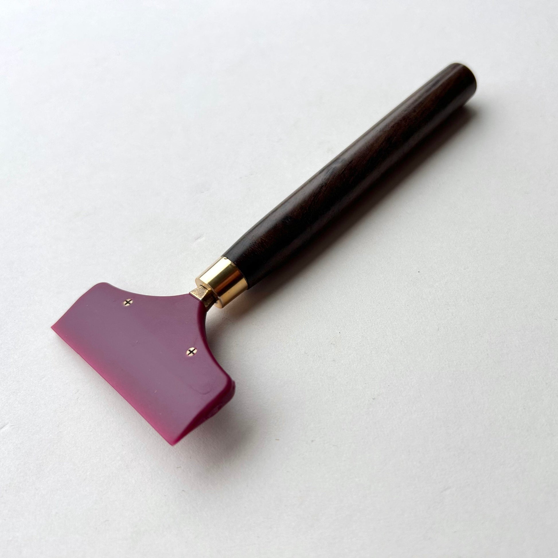 Leather glue spreader tool with purple blade and black wooden handle on a white background