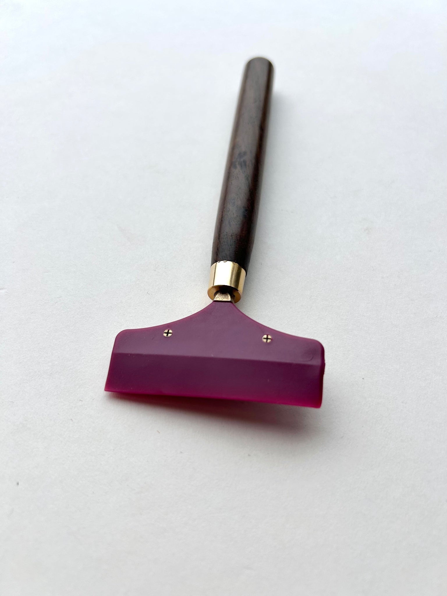 Leather glue spreader tool with purple blade and black wooden handle on a white background
