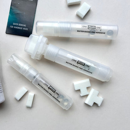 Multiple tubes of One Plus One water-based pro adhesive on a light surface with scattered adhesive pads.