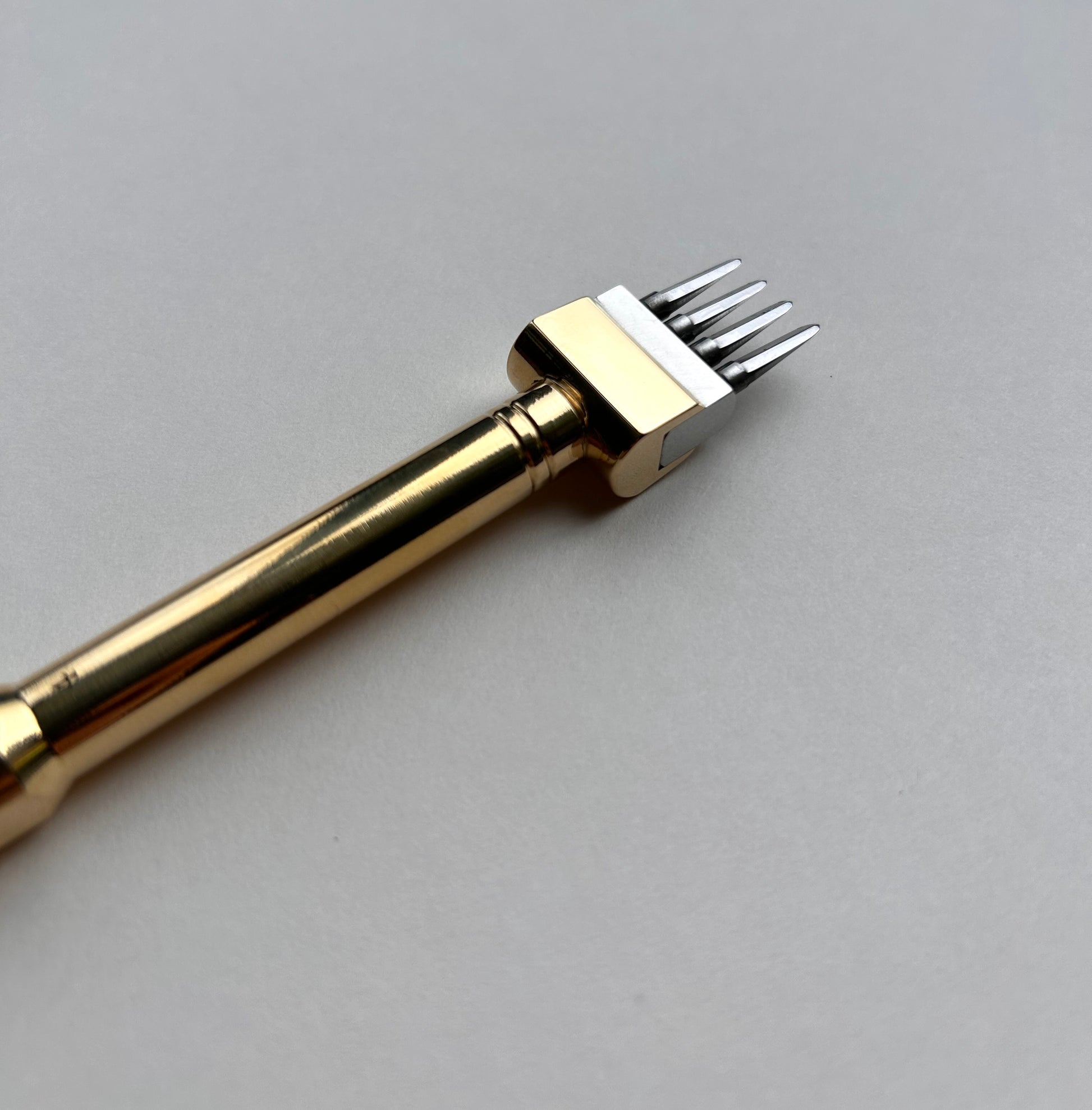 Gold-colored Sinabroks leather pricking iron tool on a light gray background