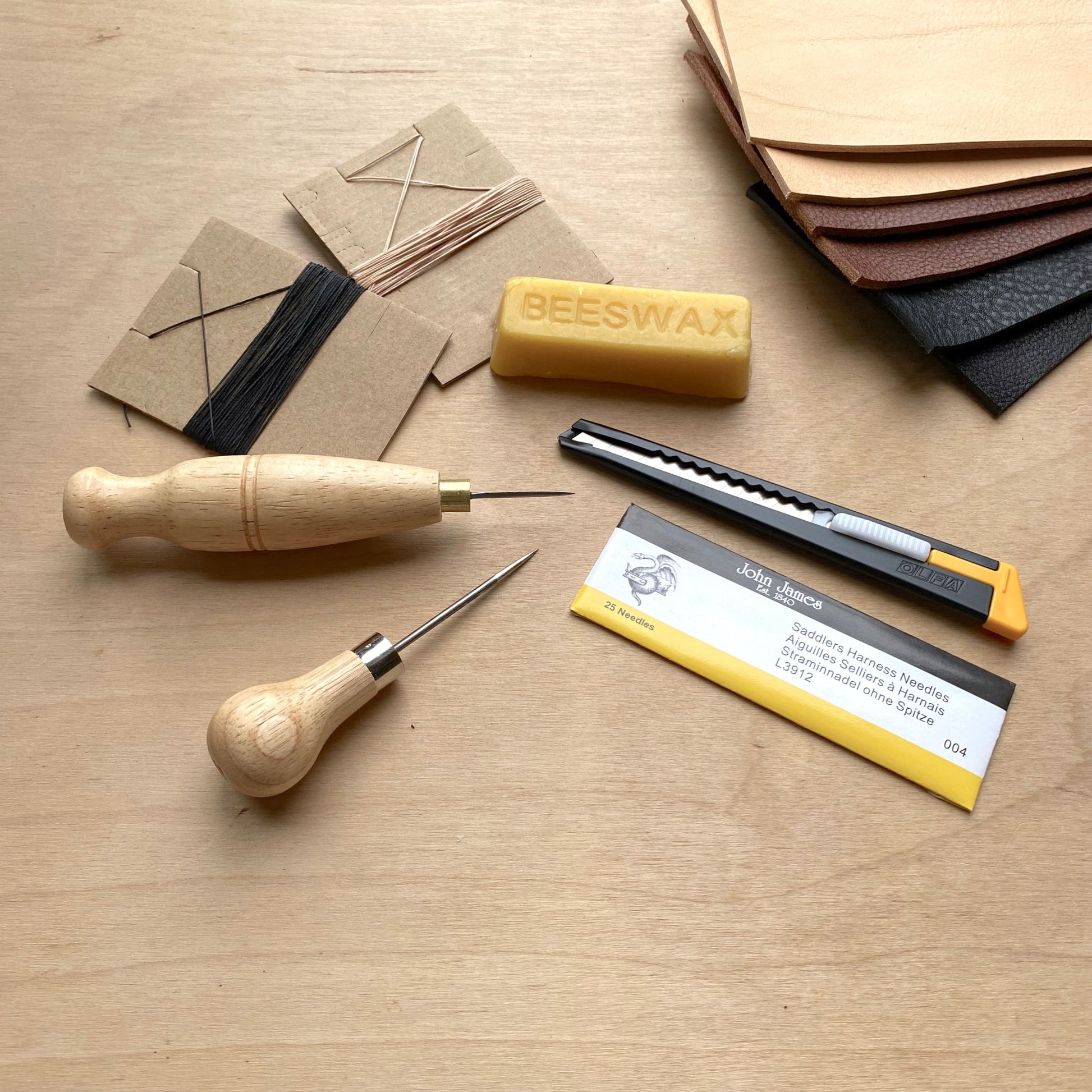 Leatherworking tools and materials including a knife, chisel, beeswax bar, and leather samples on a wooden surface.