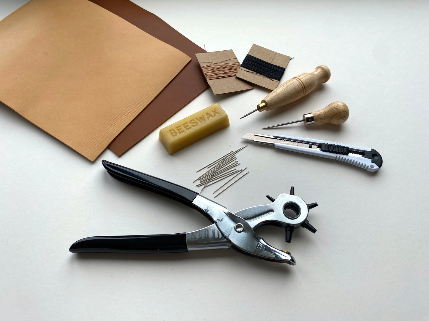 Set of tools and materials for leatherworking on a white surface
