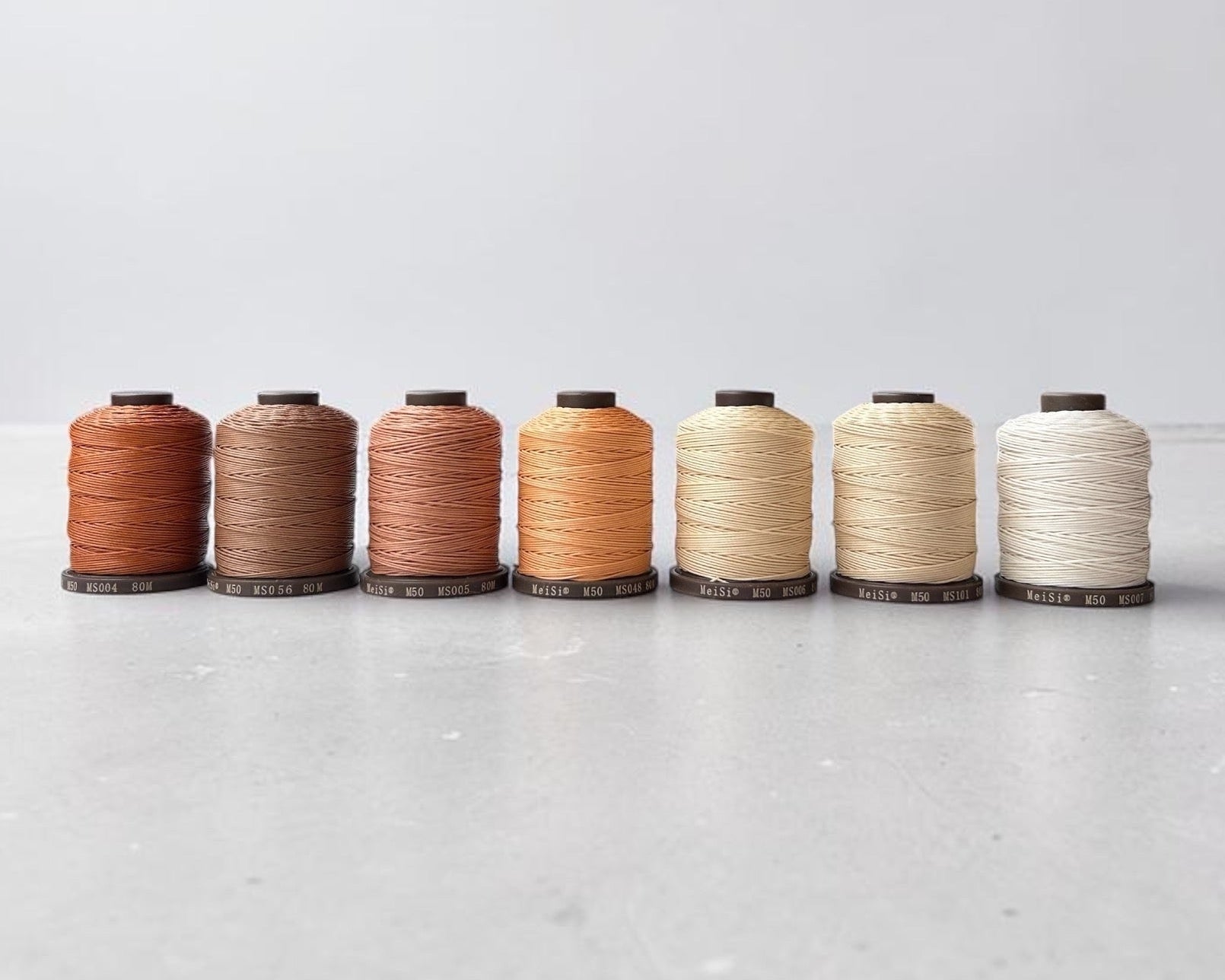 Set of six spools of Meisi Super Fine premium linen thread in various colours on a light background