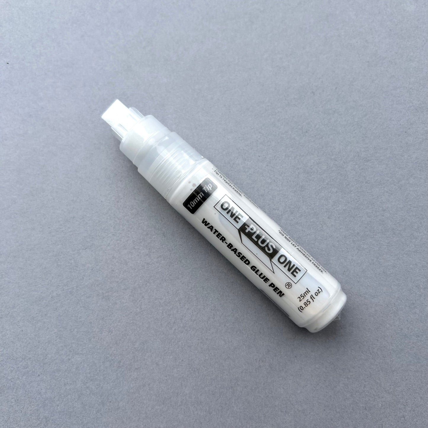 White glue pen with 'Plus One' branding on a gray background