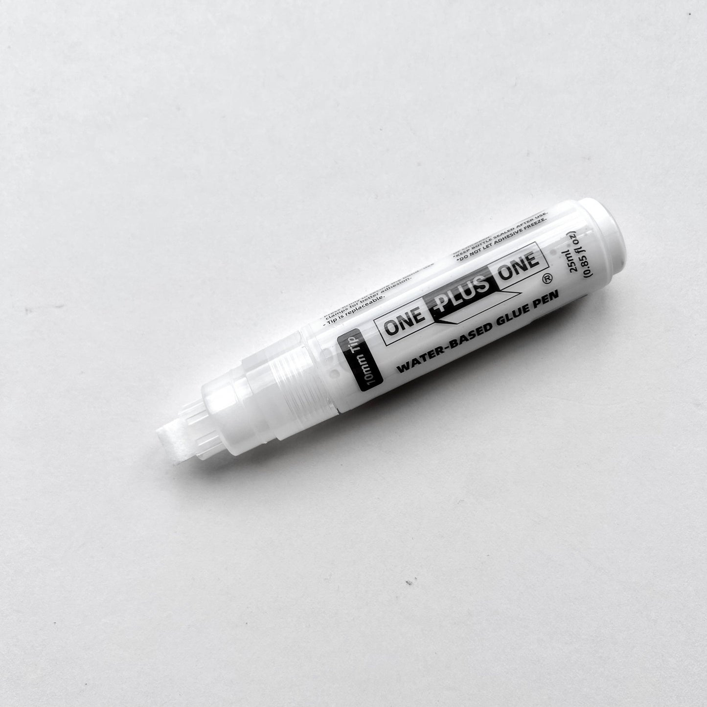 White glue pen labeled 'One Plus One' on a light gray background