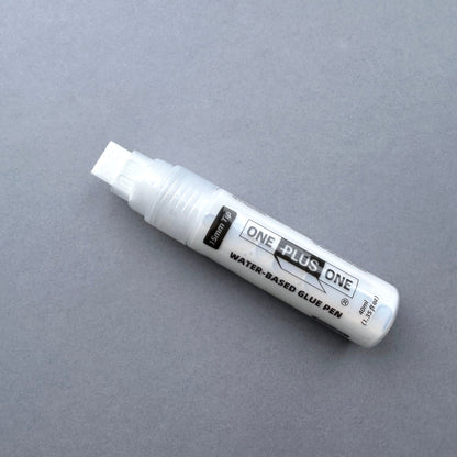 White water-based glue pen labeled 'ONE PLUS ONE' on a gray background