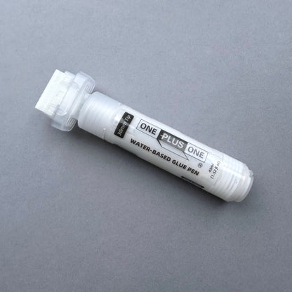 White water-based glue pen labeled 'One Plus One' on a gray background