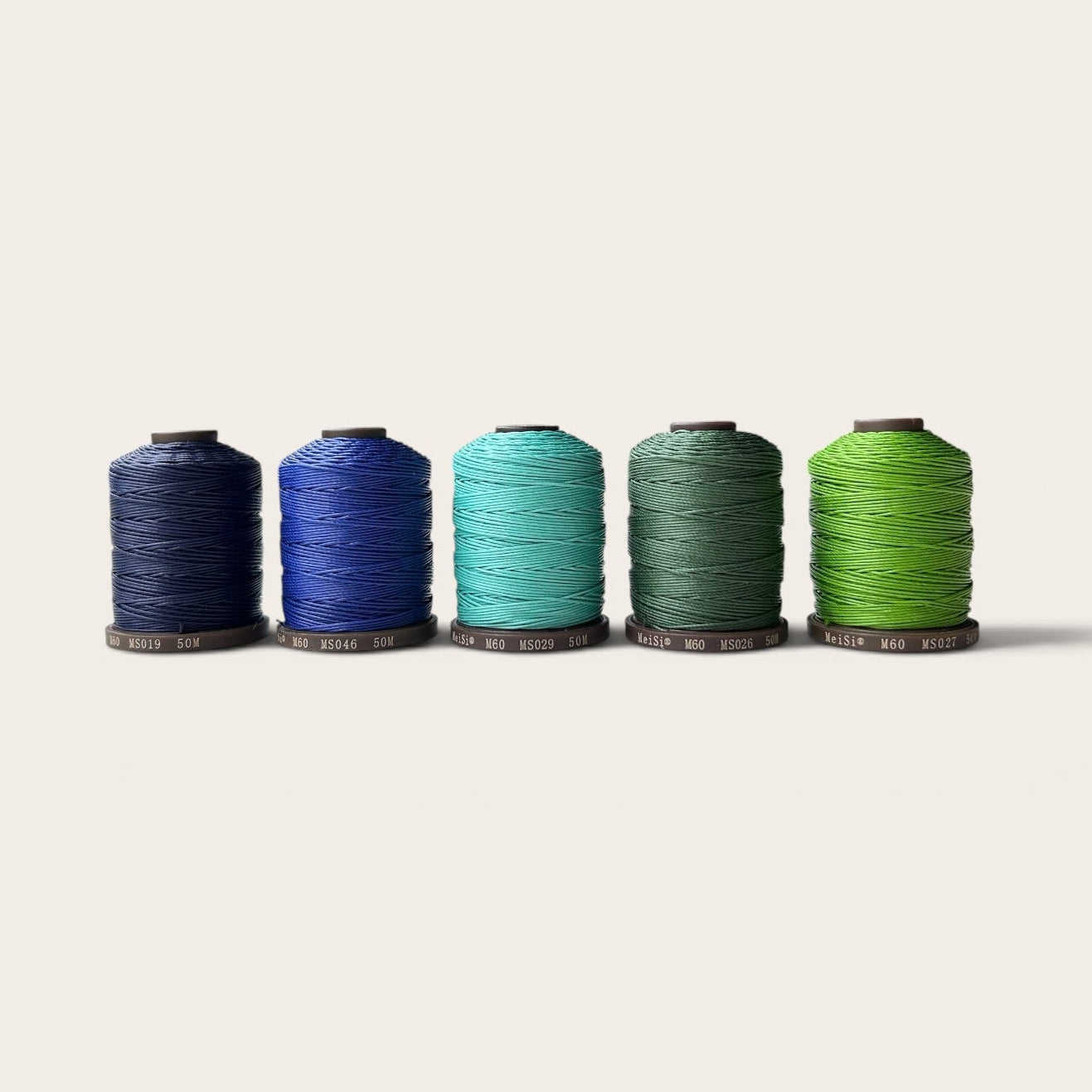 Five spools of Meisi thread in blue and green shades on a white background