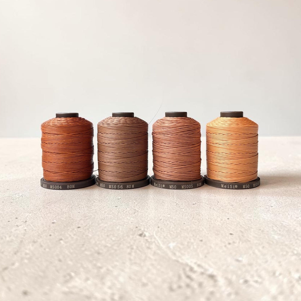 Four spools of Meisi Super Fine Linen thread in different colors on a textured surface with a light background