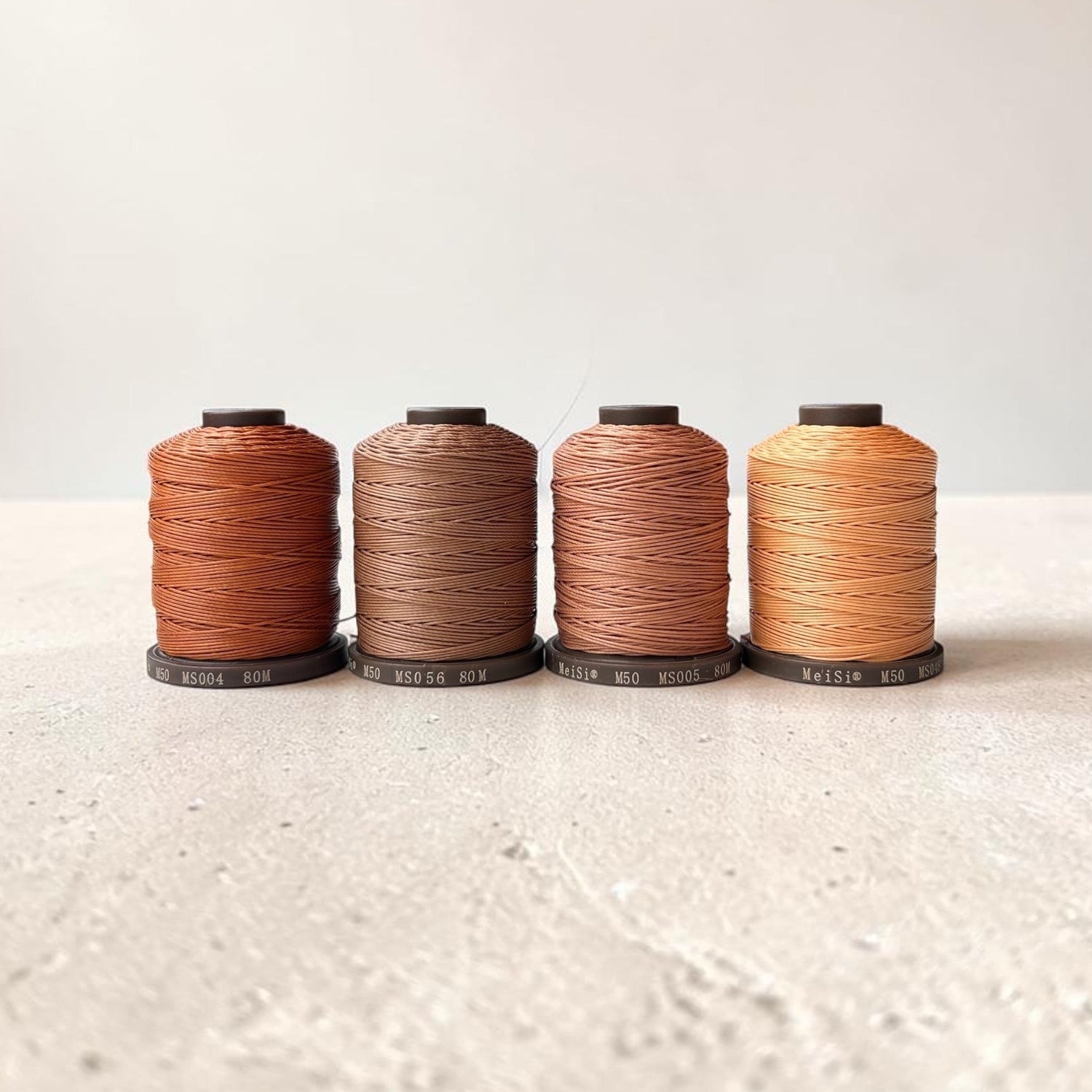 Four spools of Meisi Super Fine Linen thread in different colors on a textured surface with a light background