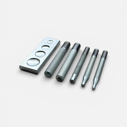 Set of metal tools for setting poppers and snaps into leather and a rectangular metal anvil on a white background