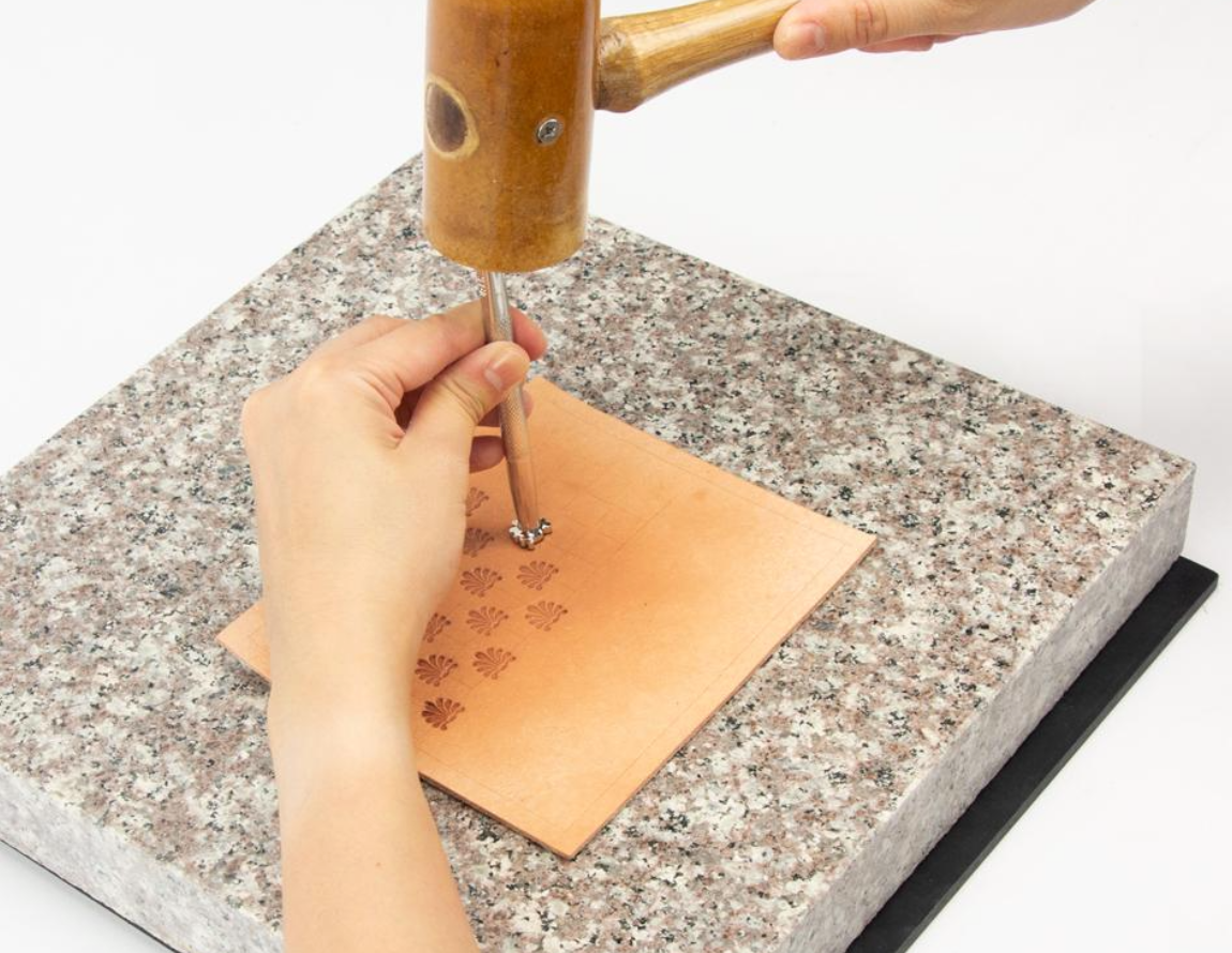Person using a leather stamp on a marble board sitting on top of a black poundo board for leathercraft 