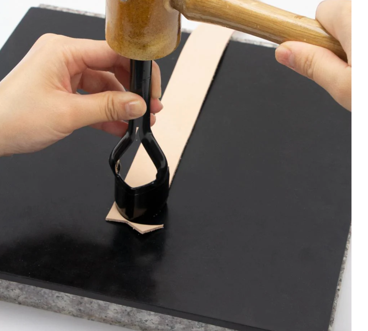 Person punching a piece of leather onto a black poundo board for leathercraft 