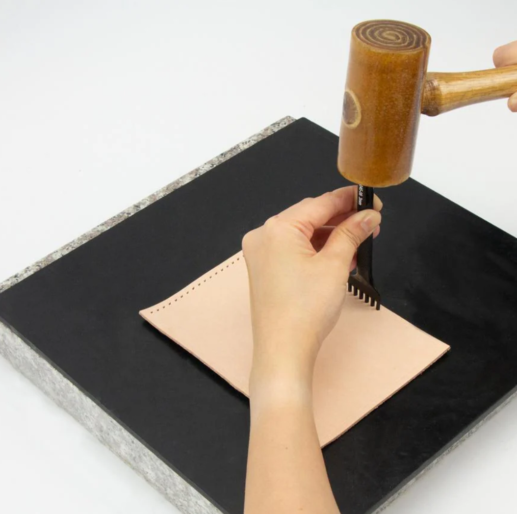 Person punching a piece of leather onto a black poundo board for leathercraft 
