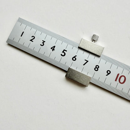 A silver metal sliding caliper or ruler scale shown on a plain white background, with black measurement markings and a red '10' visible.