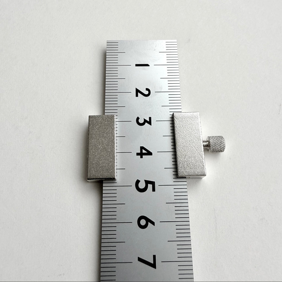 A silver metal slide ruler or caliper with a knurled adjustment knob, shown against a plain white background with a centimeter scale visible.
