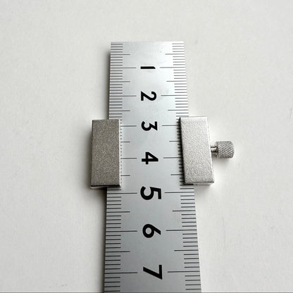 A silver metal slide ruler or caliper with a knurled adjustment knob, shown against a plain white background with a centimeter scale visible.