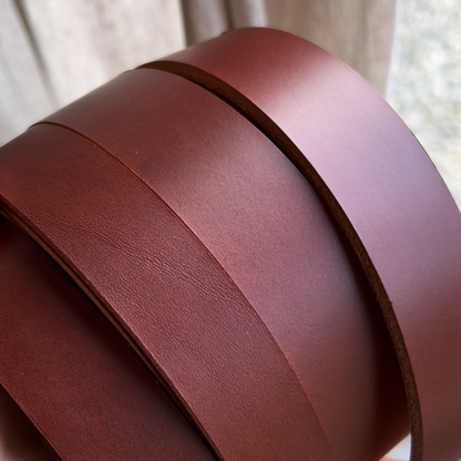Brown leather belt blank held by a hand with a neutral background