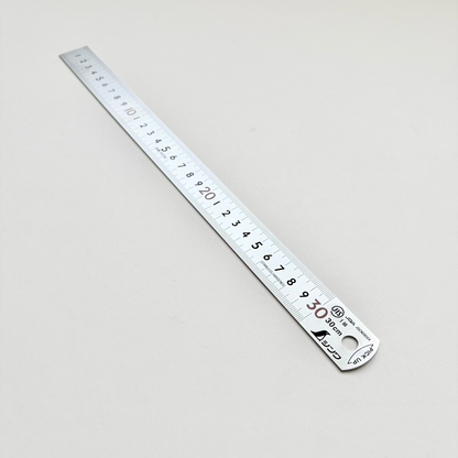 A 30 cm stainless steel ruler with black printed measurement markings and a round hanging hole, shown diagonally on a light gray background.