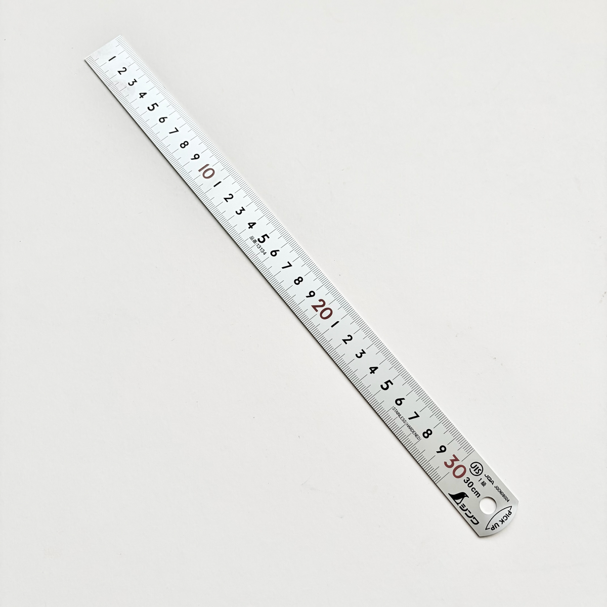 A silver metal folding ruler with black and red printed measurements, shown diagonally on a plain light gray background.