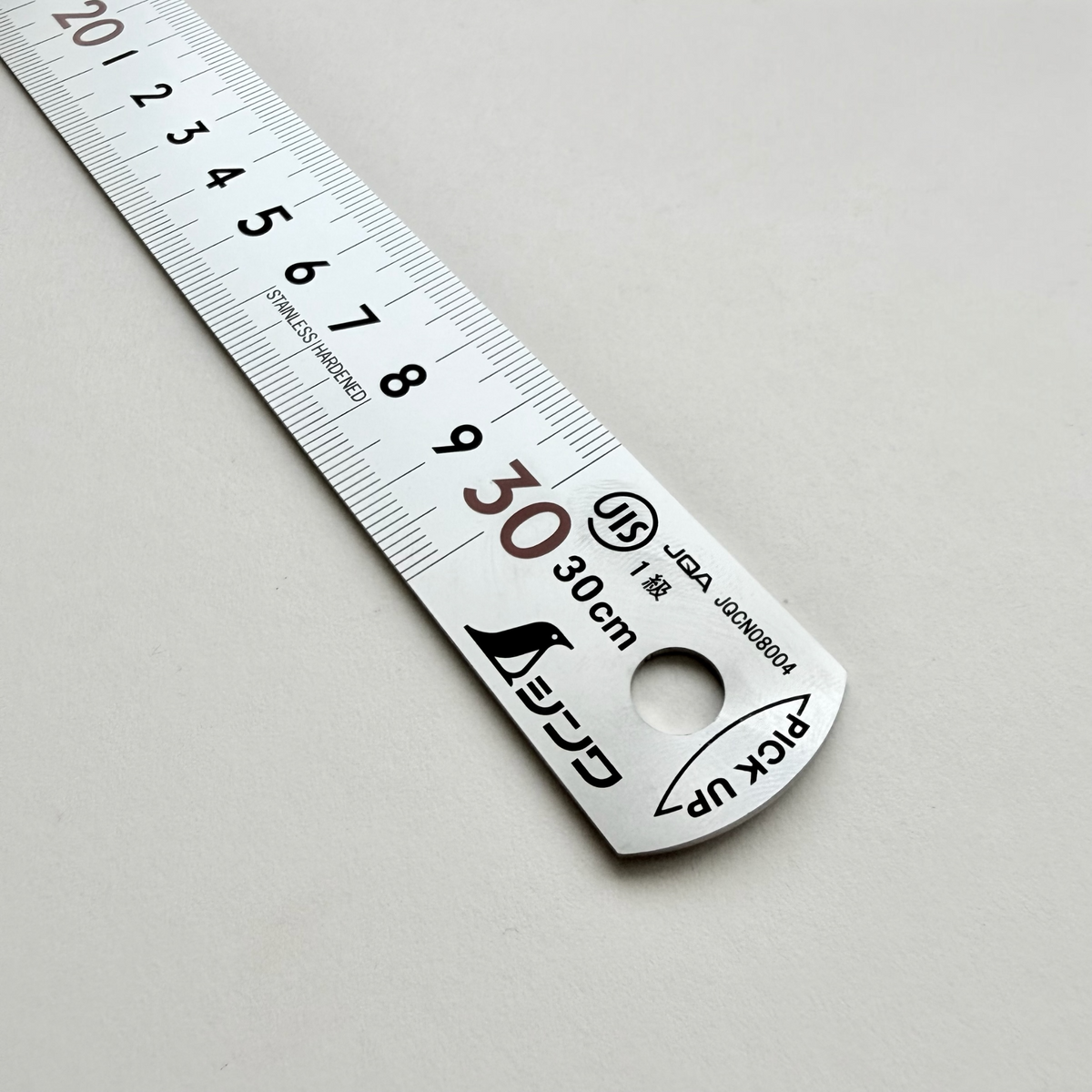 A stainless steel ruler with black printed measurements and Japanese text, photographed diagonally on a light gray background.