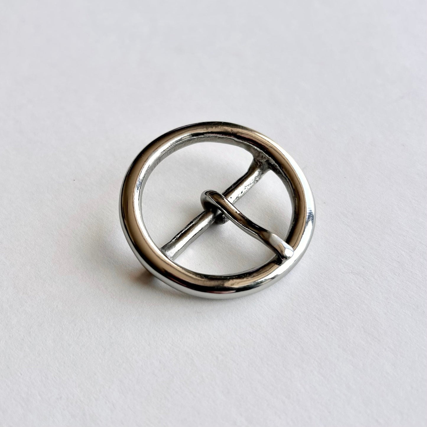 Silver metal circular buckle with a central bar on a light gray background