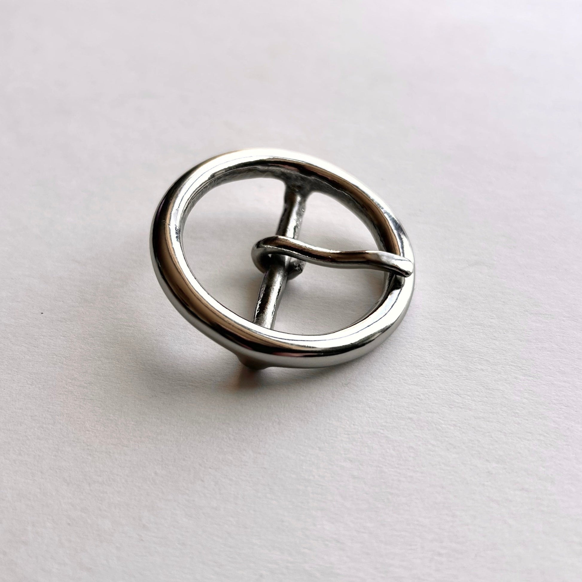 Silver metal circular buckle with a central bar on a light gray background
