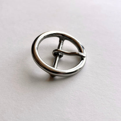 Silver metal circular buckle with a central bar on a light gray background