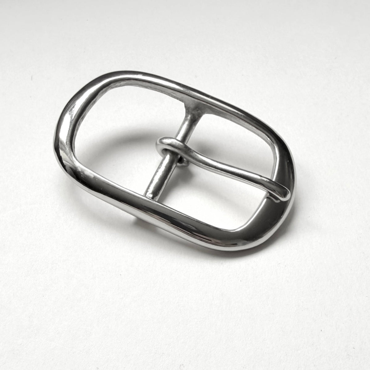 A polished silver metal belt buckle with a rounded rectangular shape and a single prong, shown on a light gray textured background.