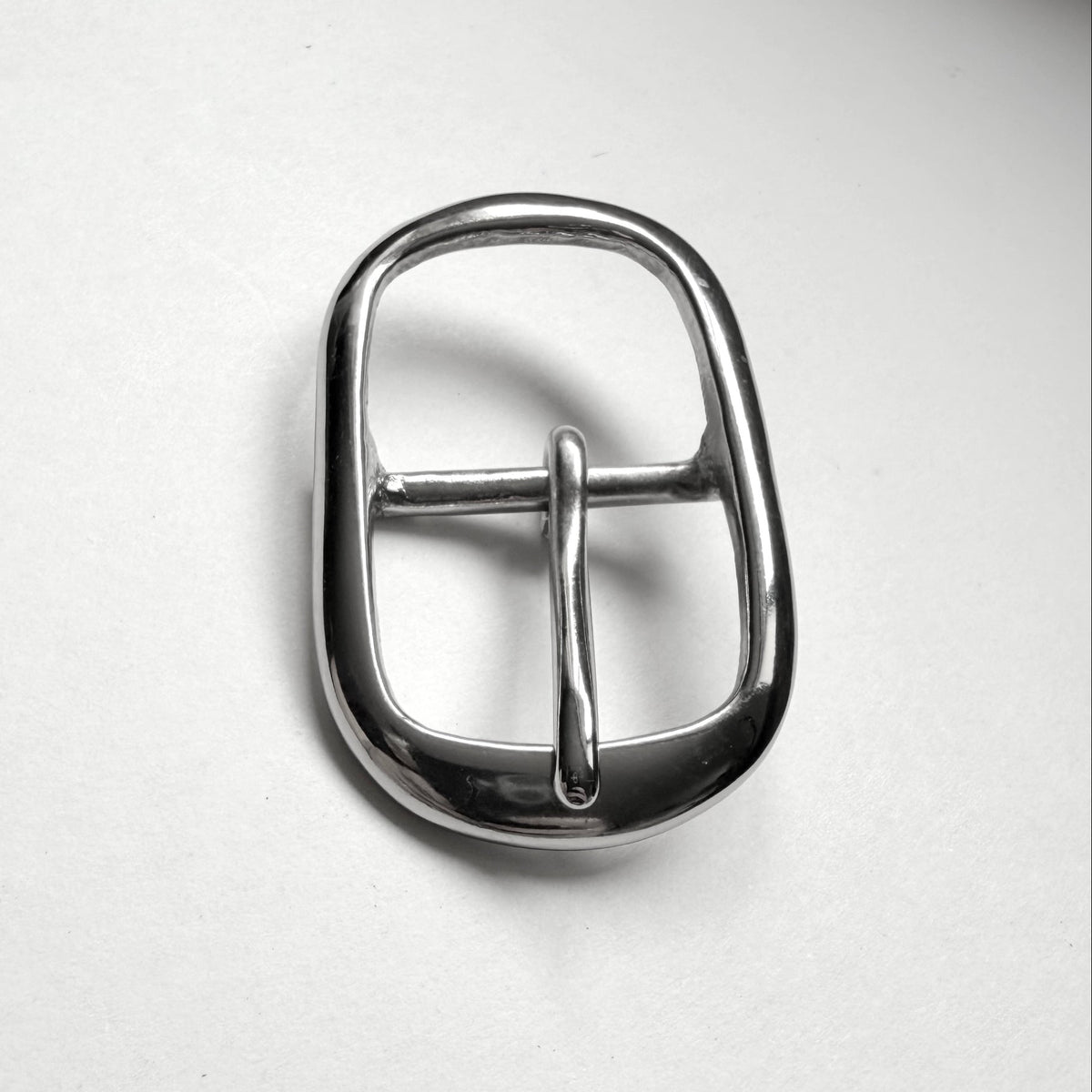 A polished silver-tone metal belt buckle with a rounded rectangular shape and a single prong, shown on a plain off-white background.
