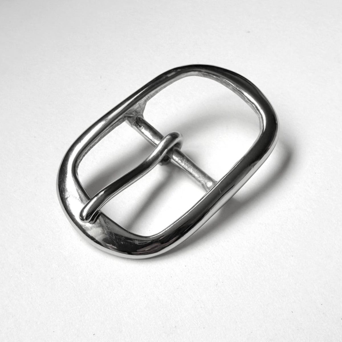 A polished silver metal belt buckle with a rounded rectangular shape and a single prong, shown on a plain light gray background.
