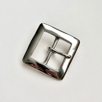A polished silver-tone metal belt buckle with a square frame and central pin, photographed on a plain light background.
