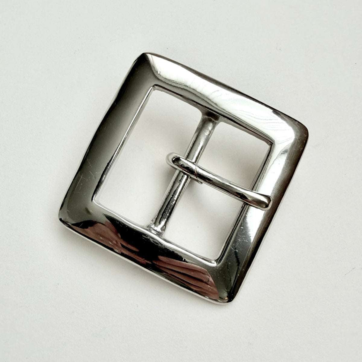 A polished silver-tone metal belt buckle with a square shape and a single prong closure, photographed on a plain light background.