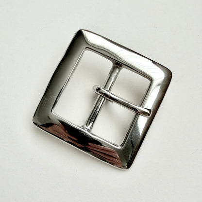 A polished silver-tone metal belt buckle with a square shape and a single prong closure, photographed on a plain light background.