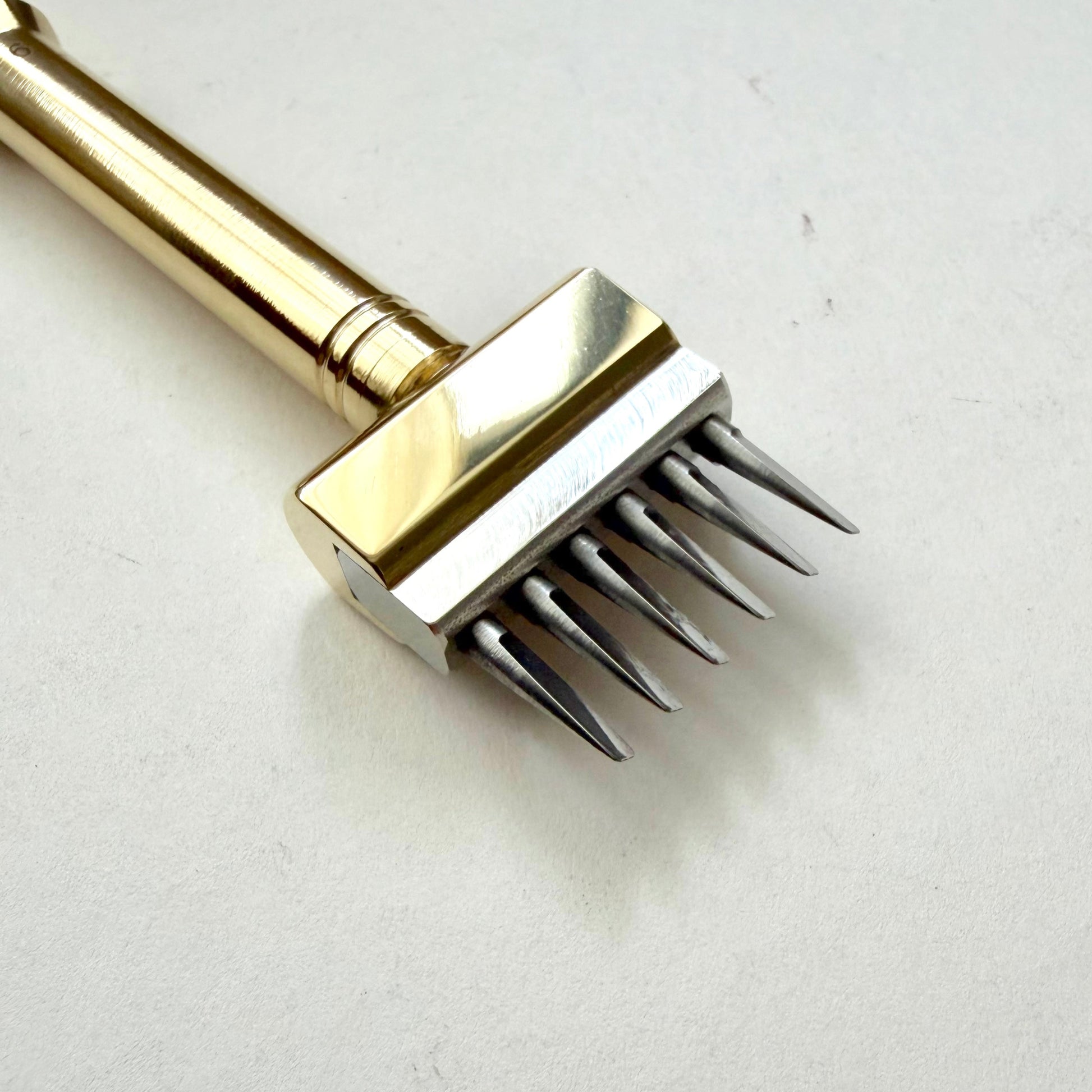 Gold coloured Sinabroks French Iron stitching punch on an off white background.