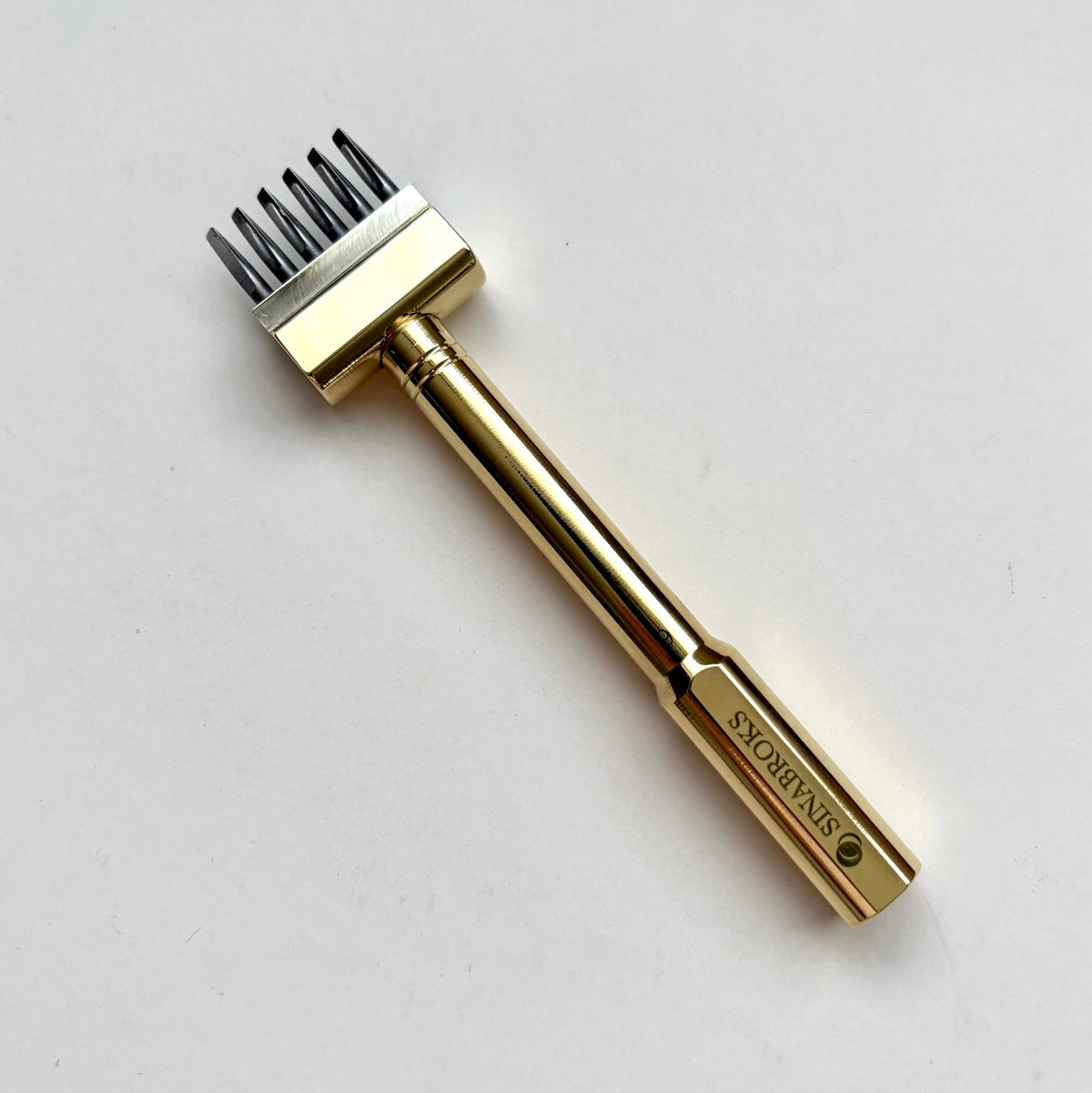 Gold coloured Sinabroks French Iron stitching punch on an off white background.
