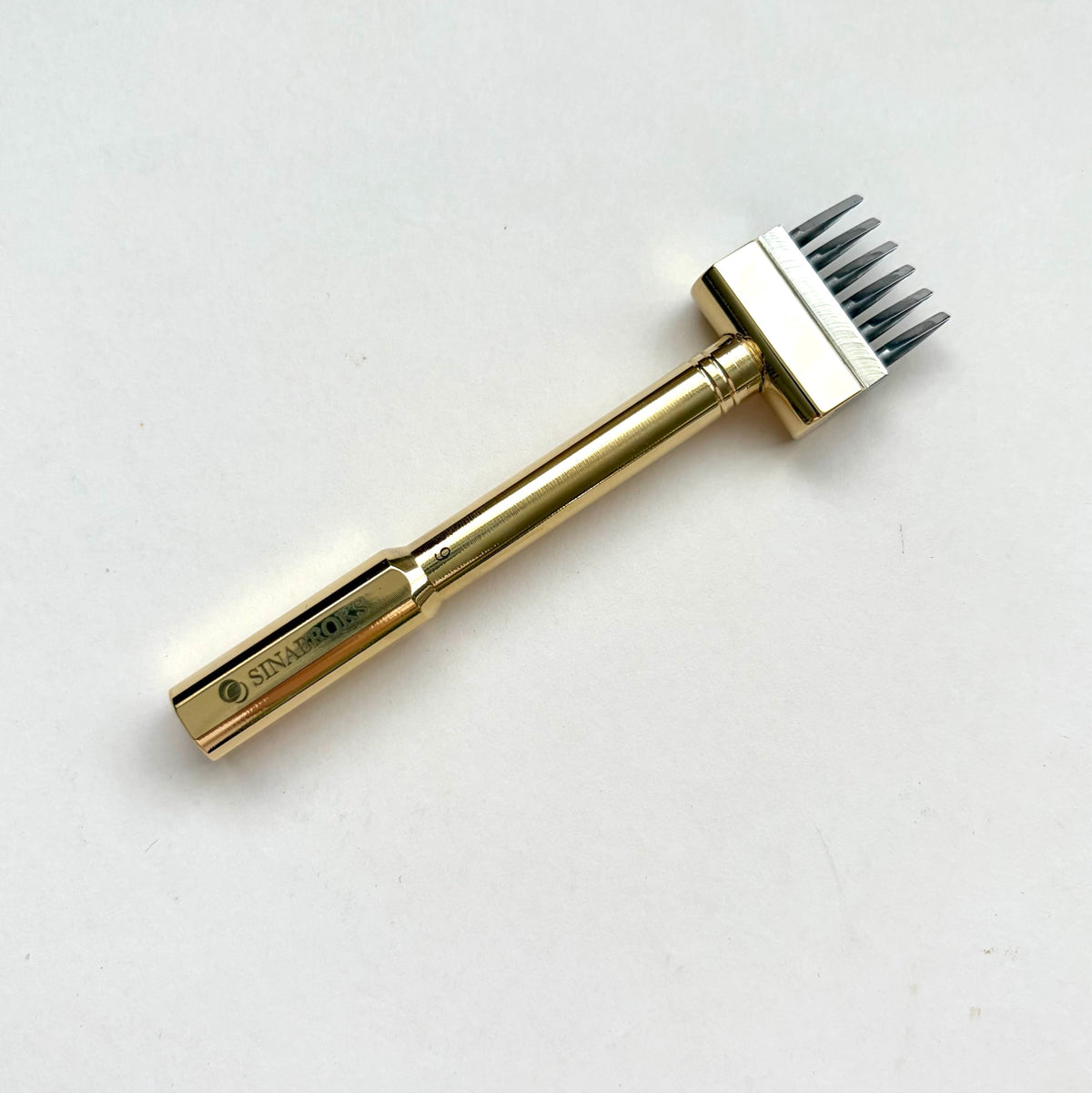 Gold coloured Sinabroks French Iron stitching punch on an off white background.