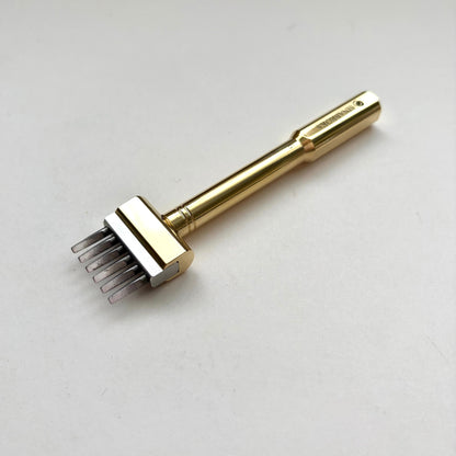 Gold coloured Sinabroks French Iron stitching punch on an off white background.