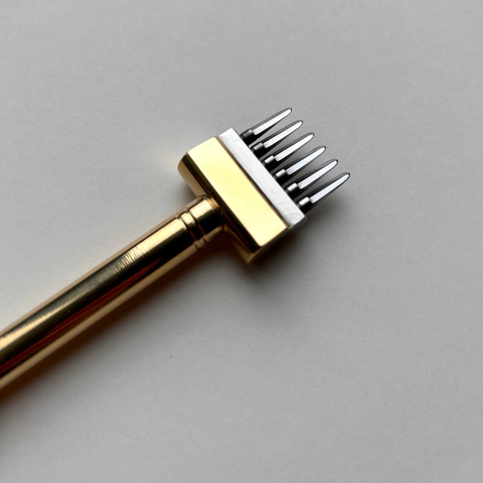 Gold-colored Sinabroks leather pricking iron tool on a light gray background