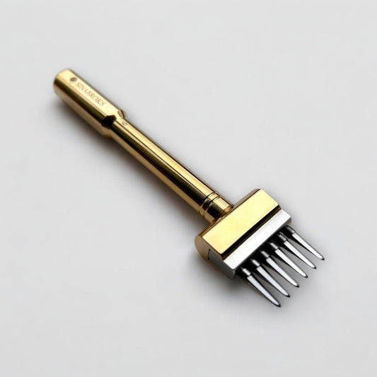 Gold-colored Sinabroks leather pricking iron tool on a light gray background