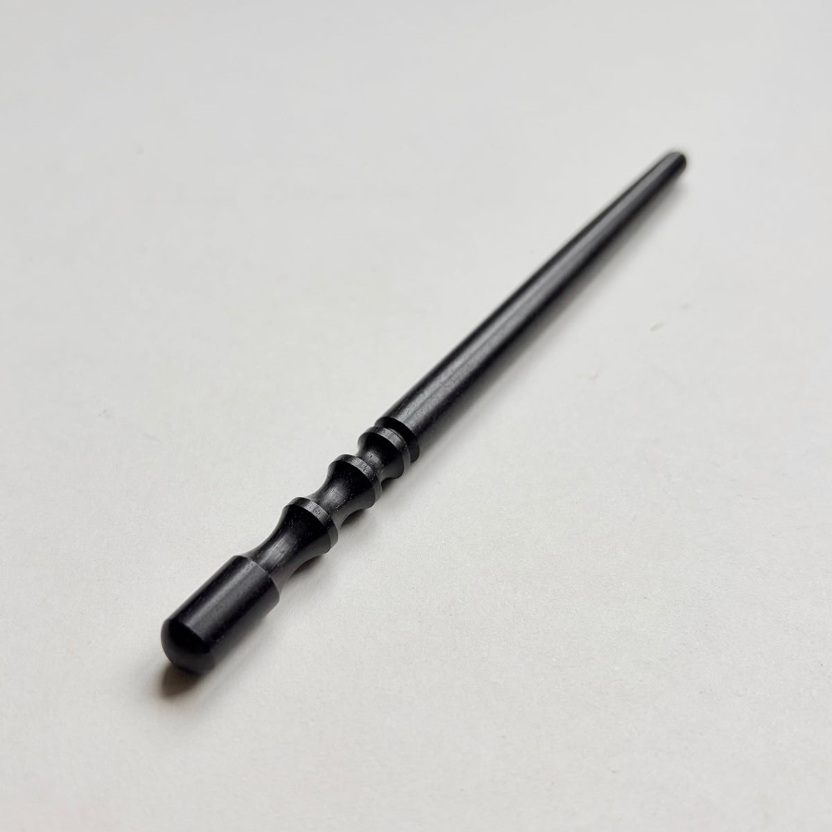 Narrow black wooden leather edge burnisher tool on a grey background