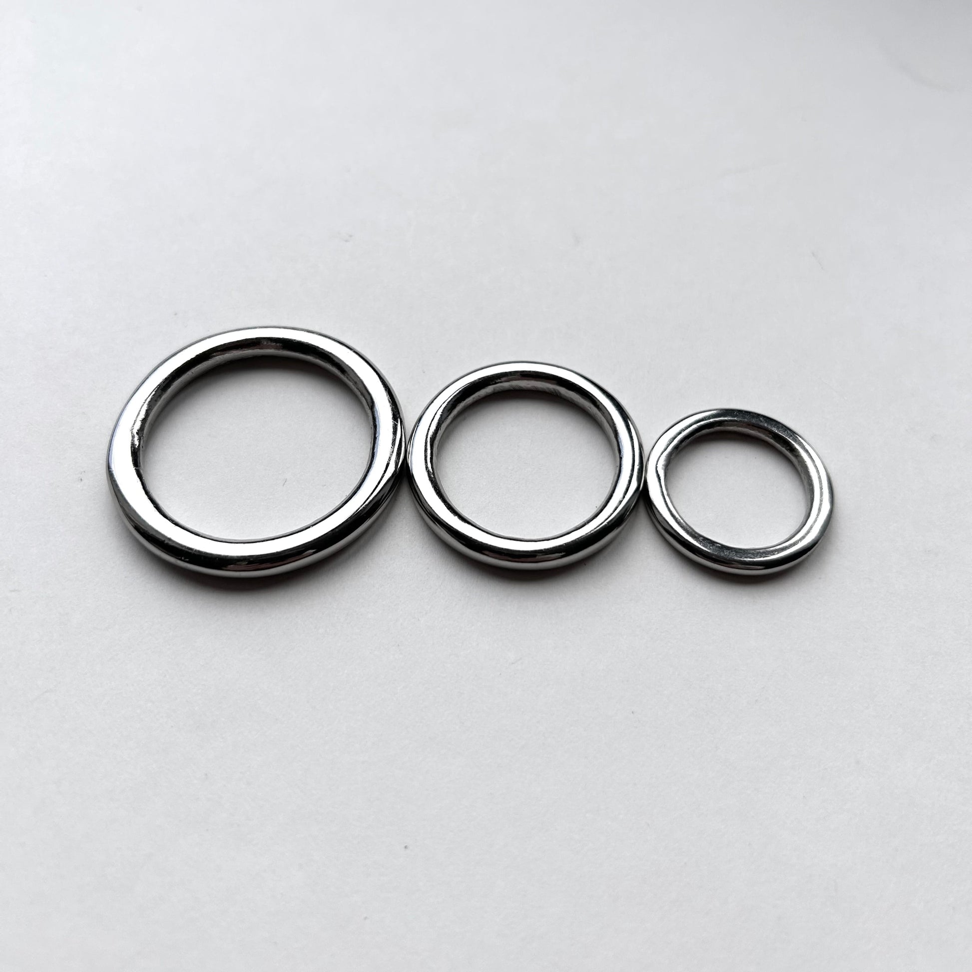 Three silver o rings for leathercraft of different sizes on a light grey background