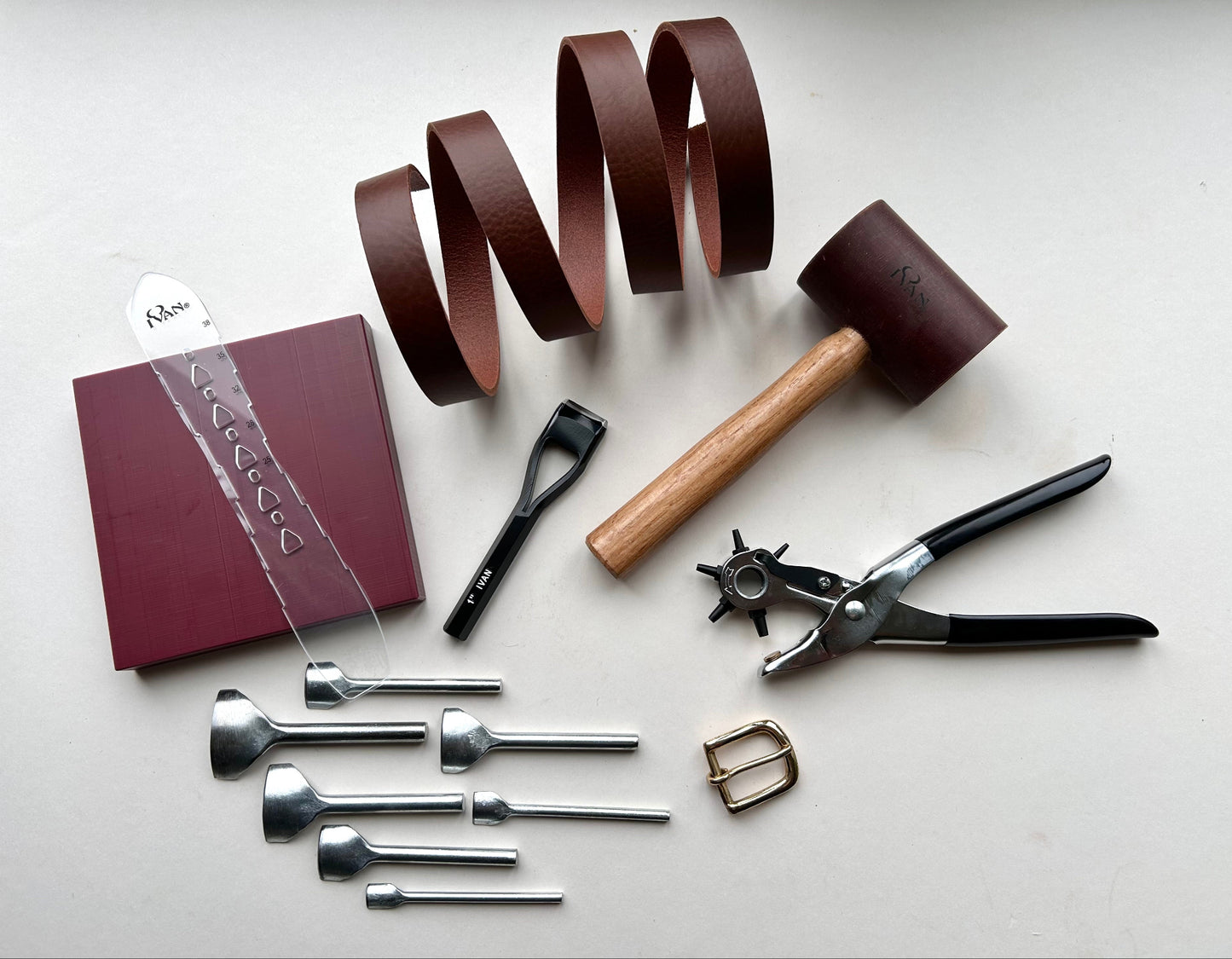 Set of leatherworking tools including a leather book, leather strips, and various tools on a light surface.