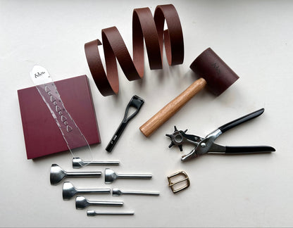 Set of leatherworking tools including a leather book, leather strips, and various tools on a light surface.