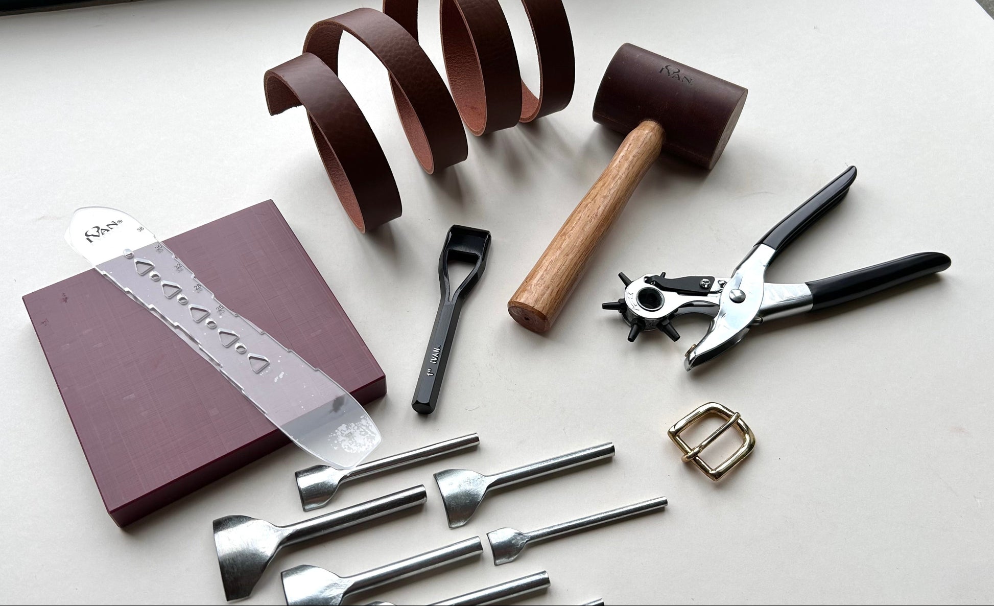 Collection of leatherworking tools and materials on a white surface